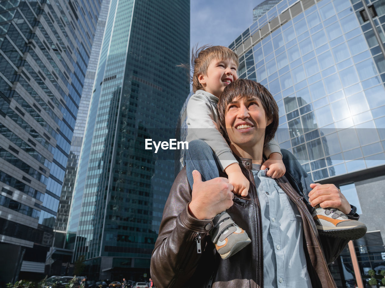 Little boy sits on father's shoulders among skyscrapers. dad and son looks on walls of buildings. 
