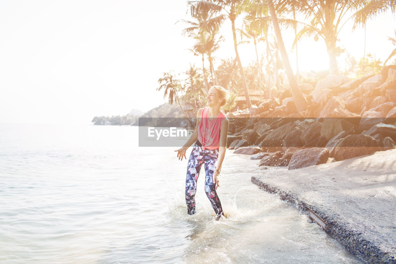 Happy mid adult woman standing at beach during sunny day