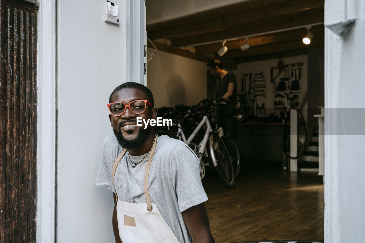 Confident male owner with funky eyeglasses looking away outside bicycle shop