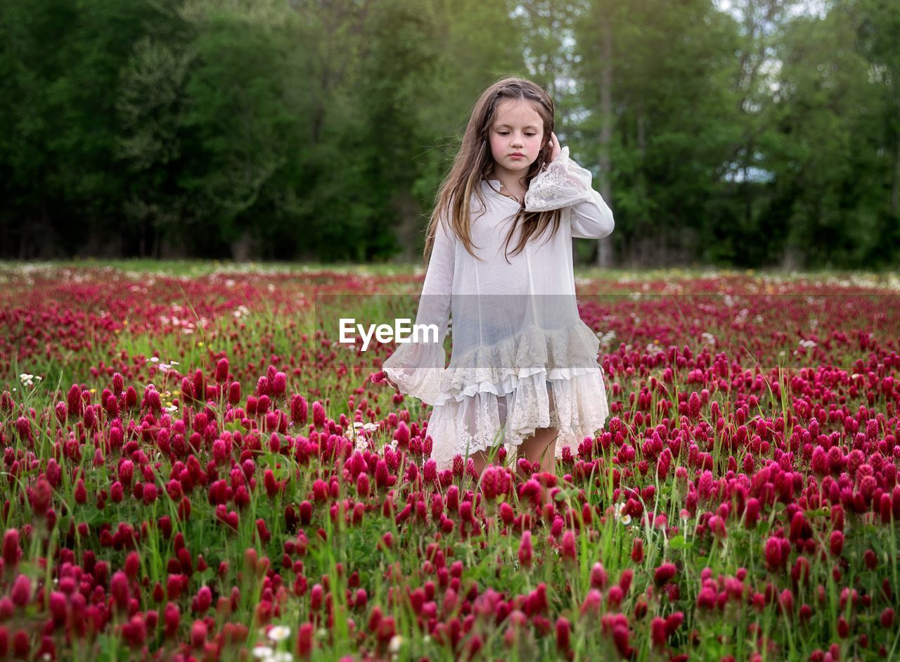 portrait of smiling young woman standing amidst flowers on field