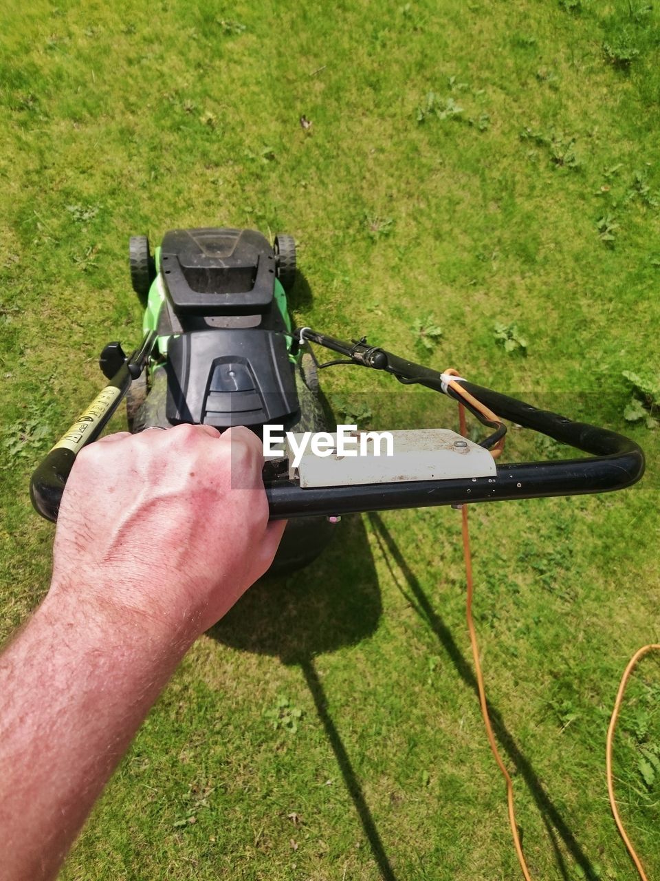 Cropped image of man using lawn mover on grassy field