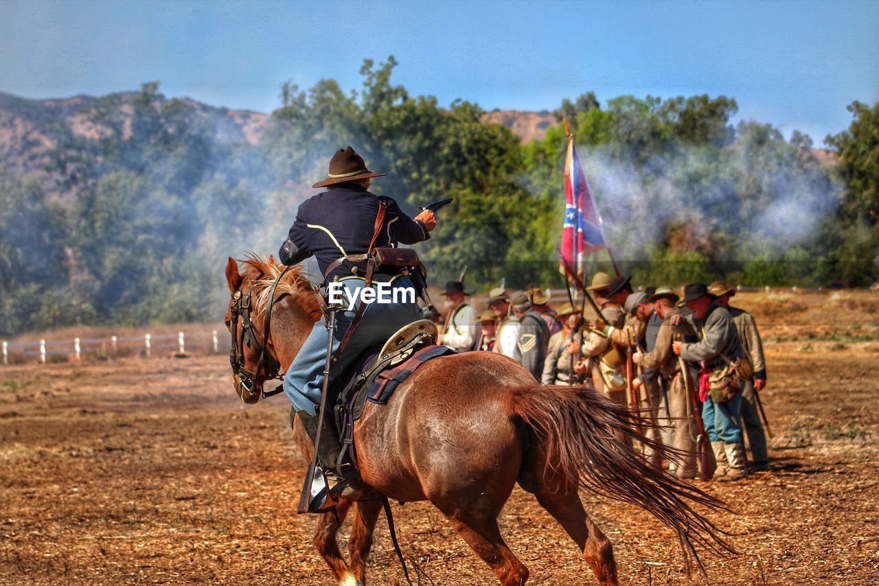 REAR VIEW OF PEOPLE RIDING HORSE CART ON FIELD