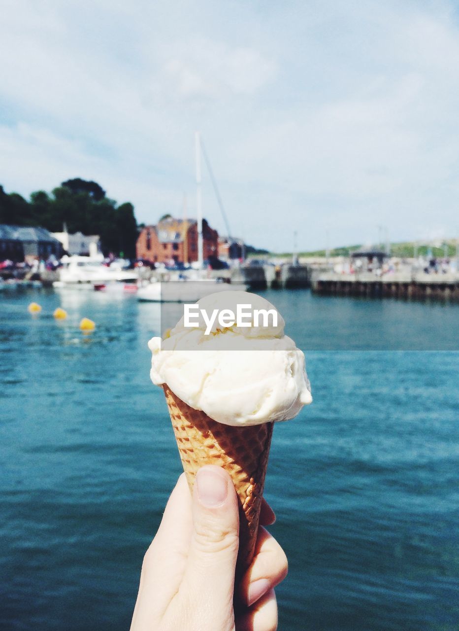 Close-up of hand holding ice cream cone against lake