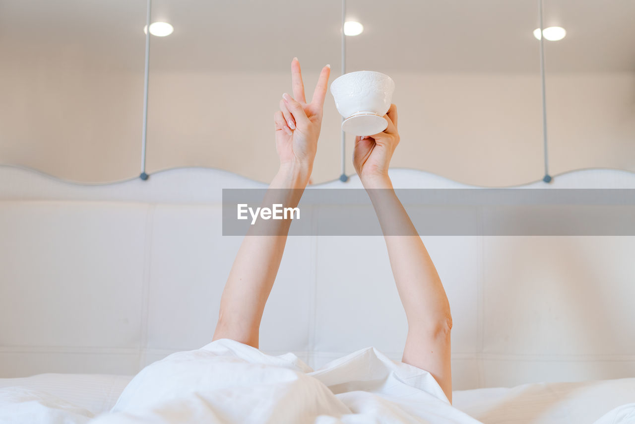 Young woman with a coffee mug in bed with white linens. minimal happy morning