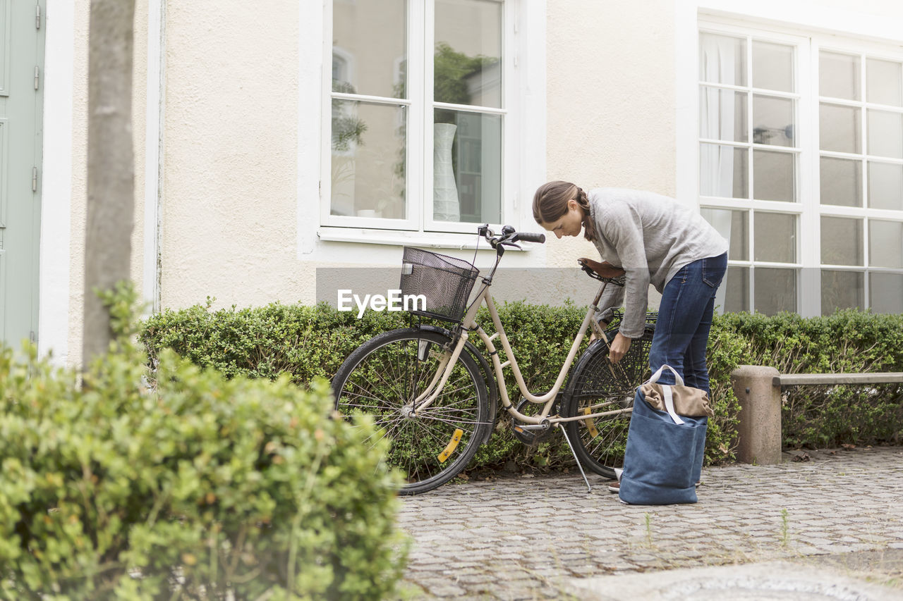 Woman locking bicycle by plants outside house