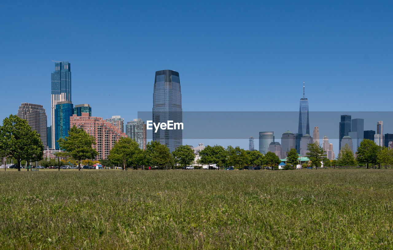 Scenic view of field by modern buildings against clear sky