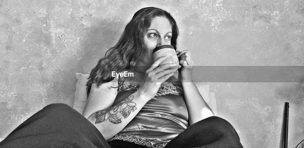 Low angle view of woman drinking coffee while sitting against wall