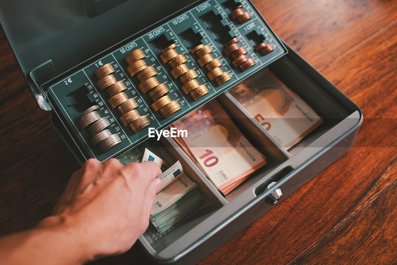 Cropped hand on mid adult man taking money from box on table