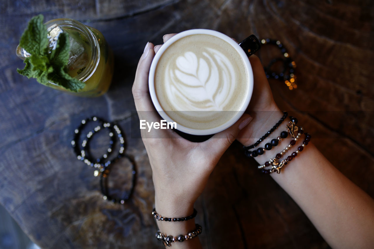 Cropped hands of woman holding coffee cup on wooden table in cafe