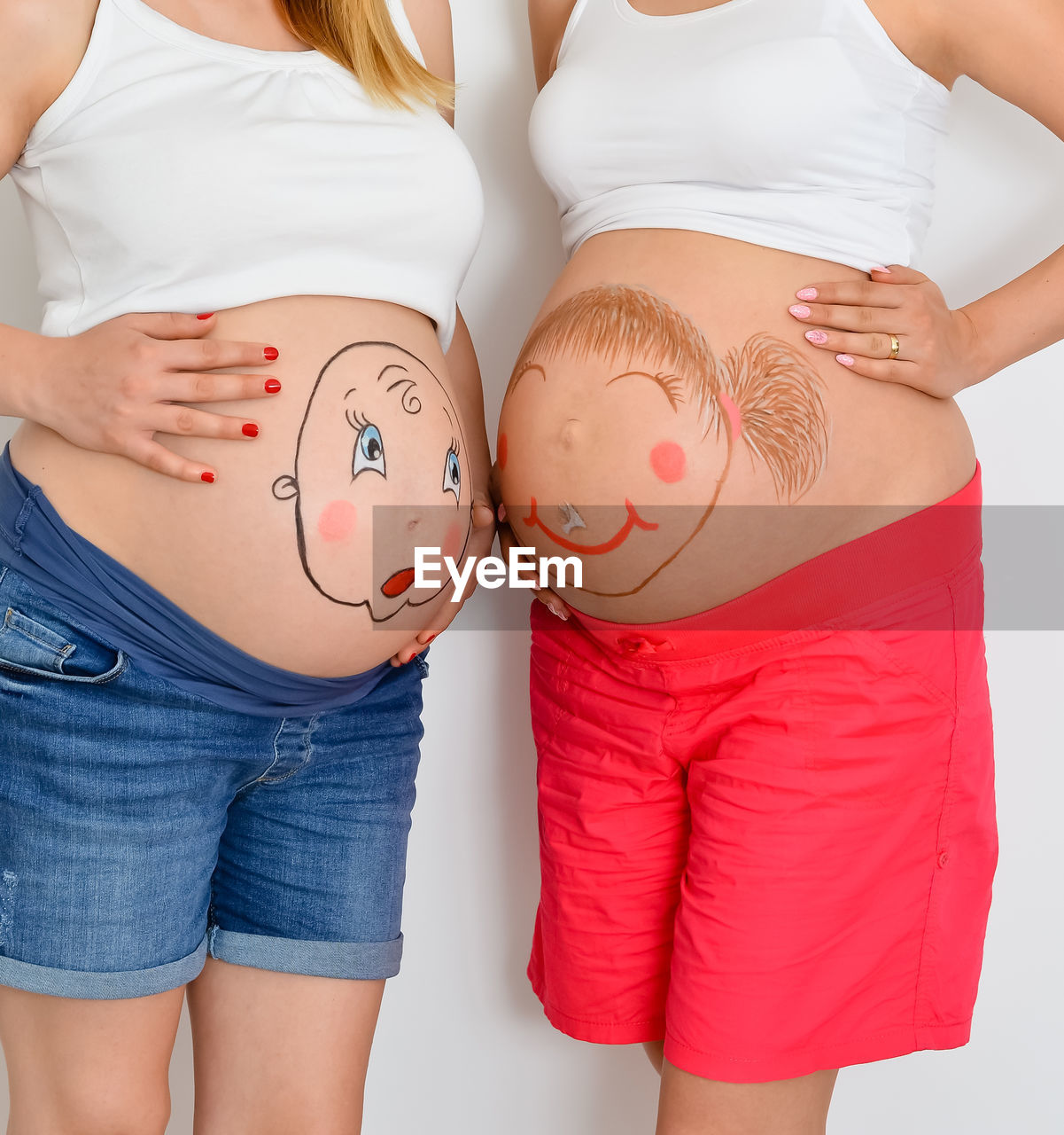 Midsection of pregnant women with painting bellies standing against white background