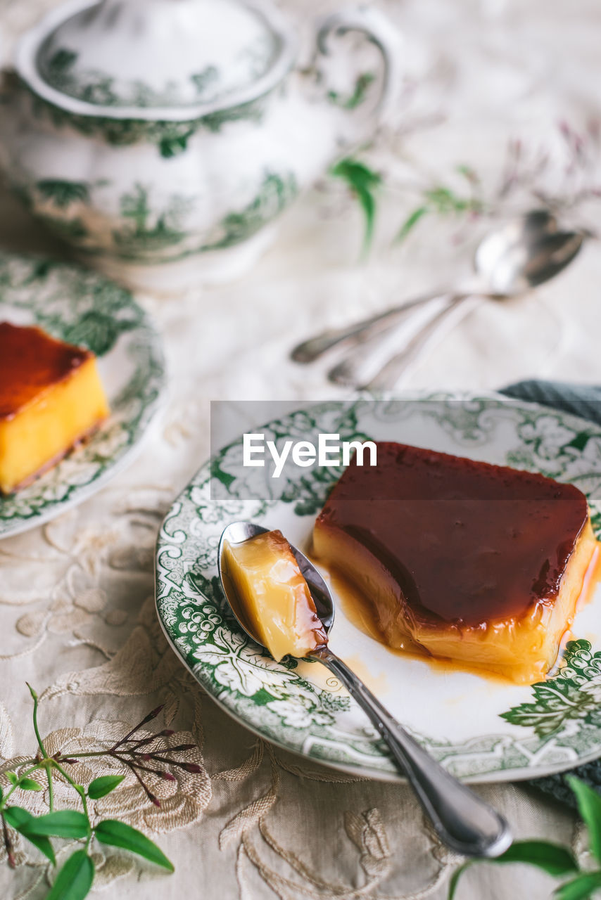 Top view of yummy caramel pudding served on ceramic plates with sauce and spoon during breakfast on table with white tablecloth
