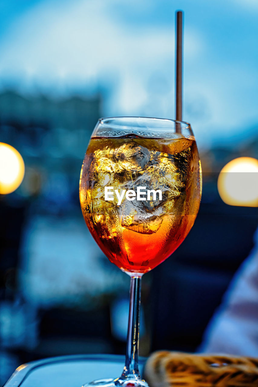 A cold alcoholic beverage aperol spritz with ice and straw against out of focus background