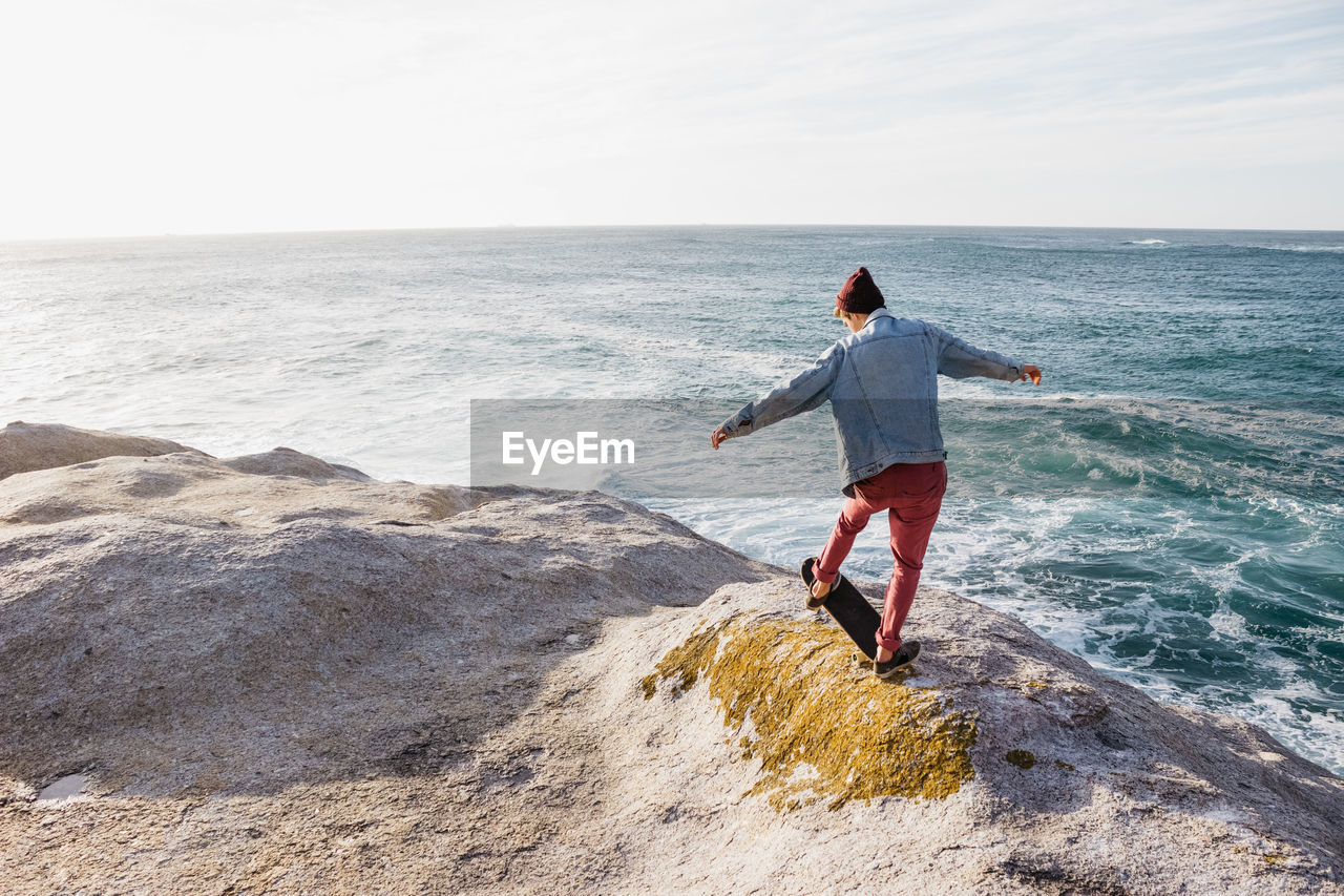 Rear view of boy on rock by sea against sky