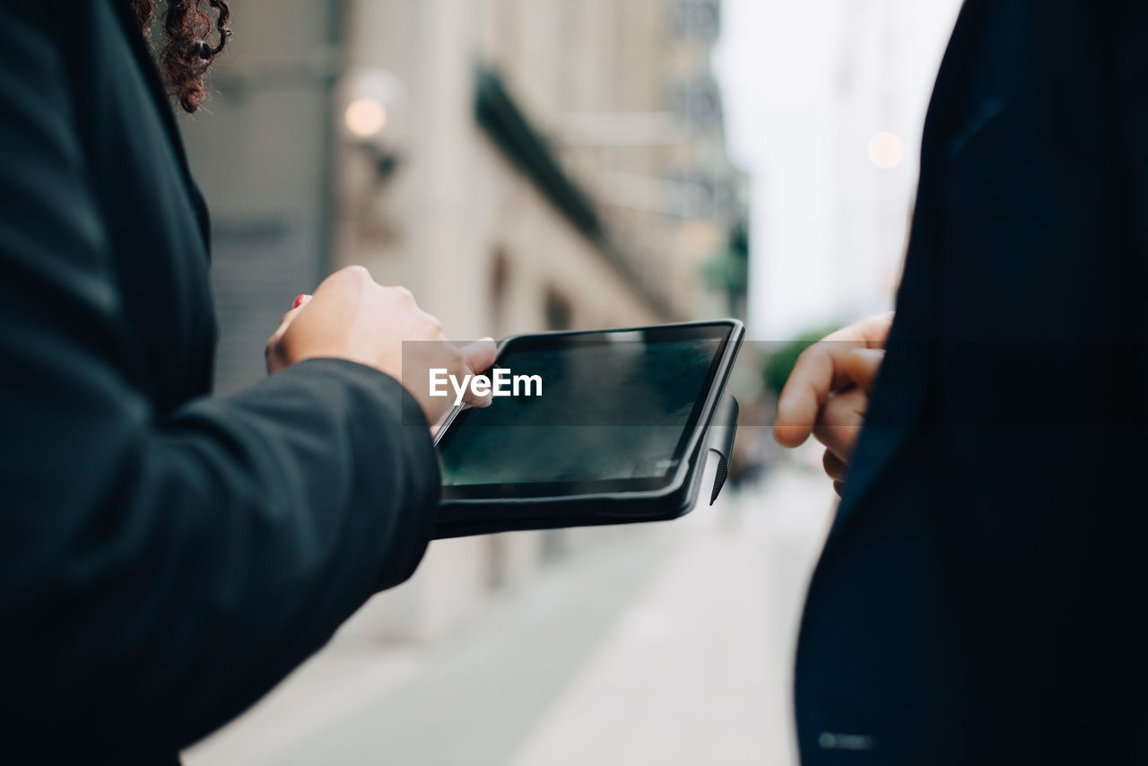 Midsection of business colleagues with digital tablet standing in city