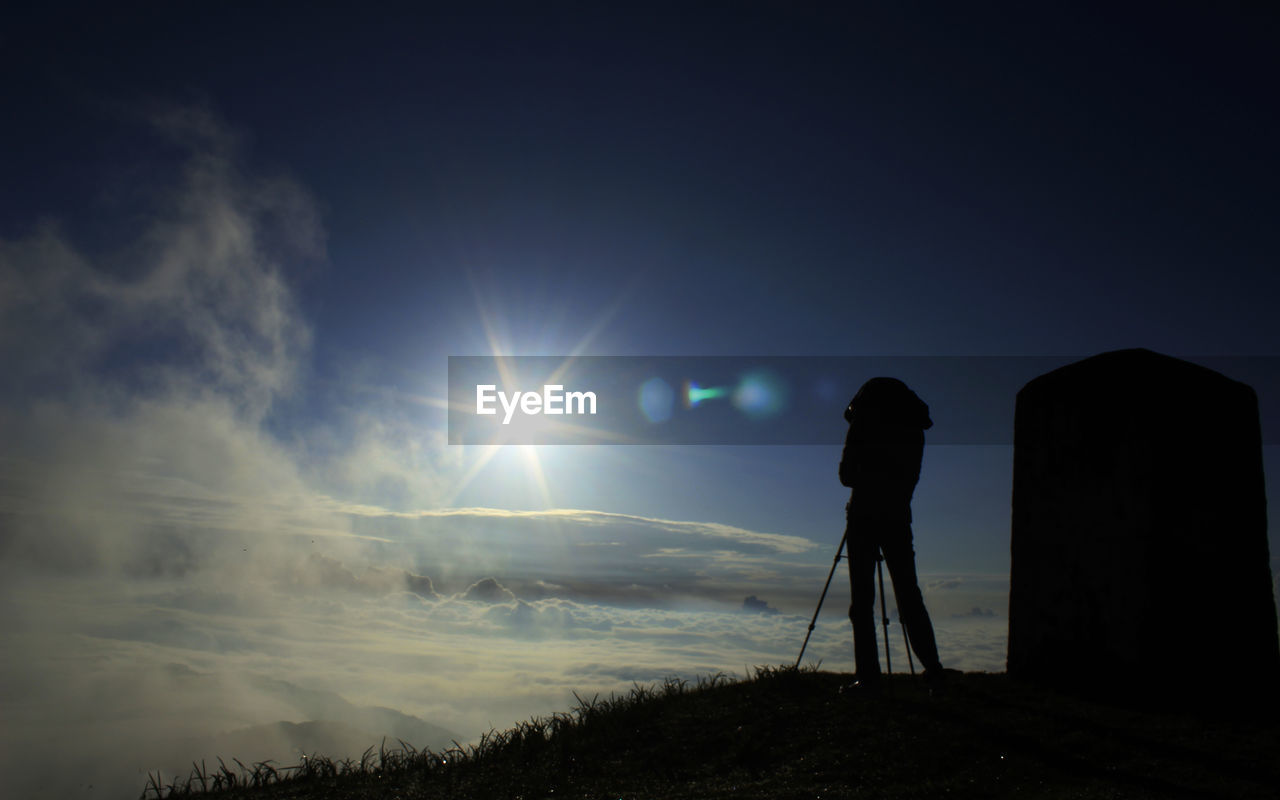 SILHOUETTE OF MAN STANDING ON MOUNTAIN PEAK