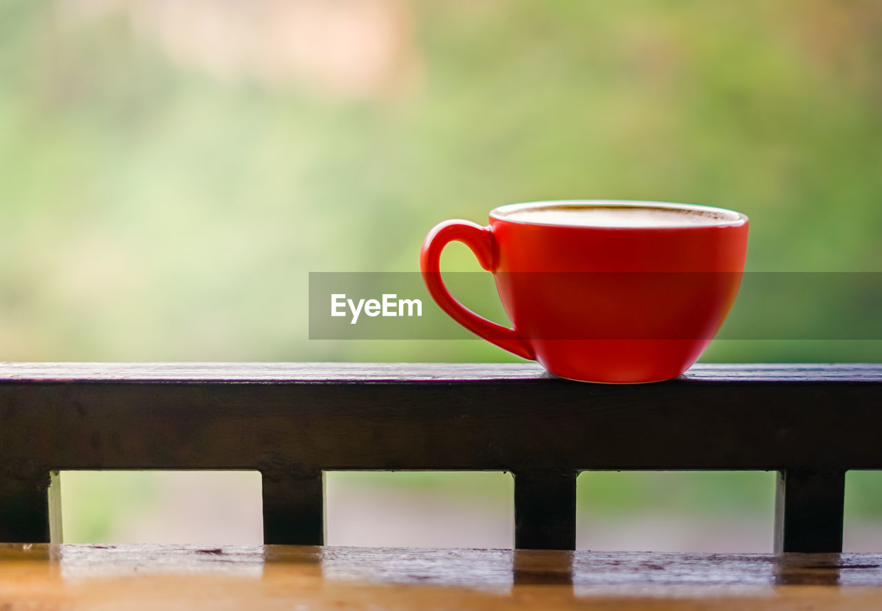 CLOSE-UP OF COFFEE CUP ON TABLE AGAINST RAILING