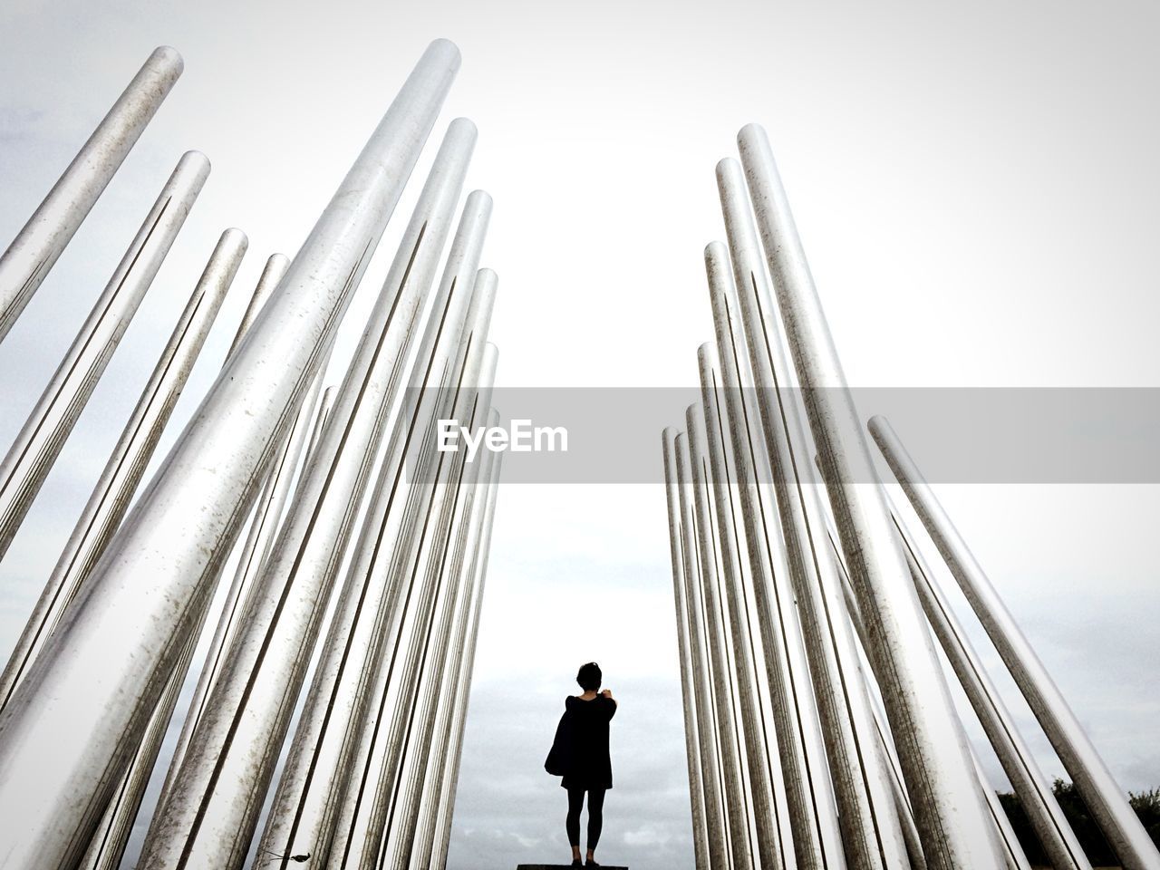 Rear view of woman standing amidst metal poles against sky