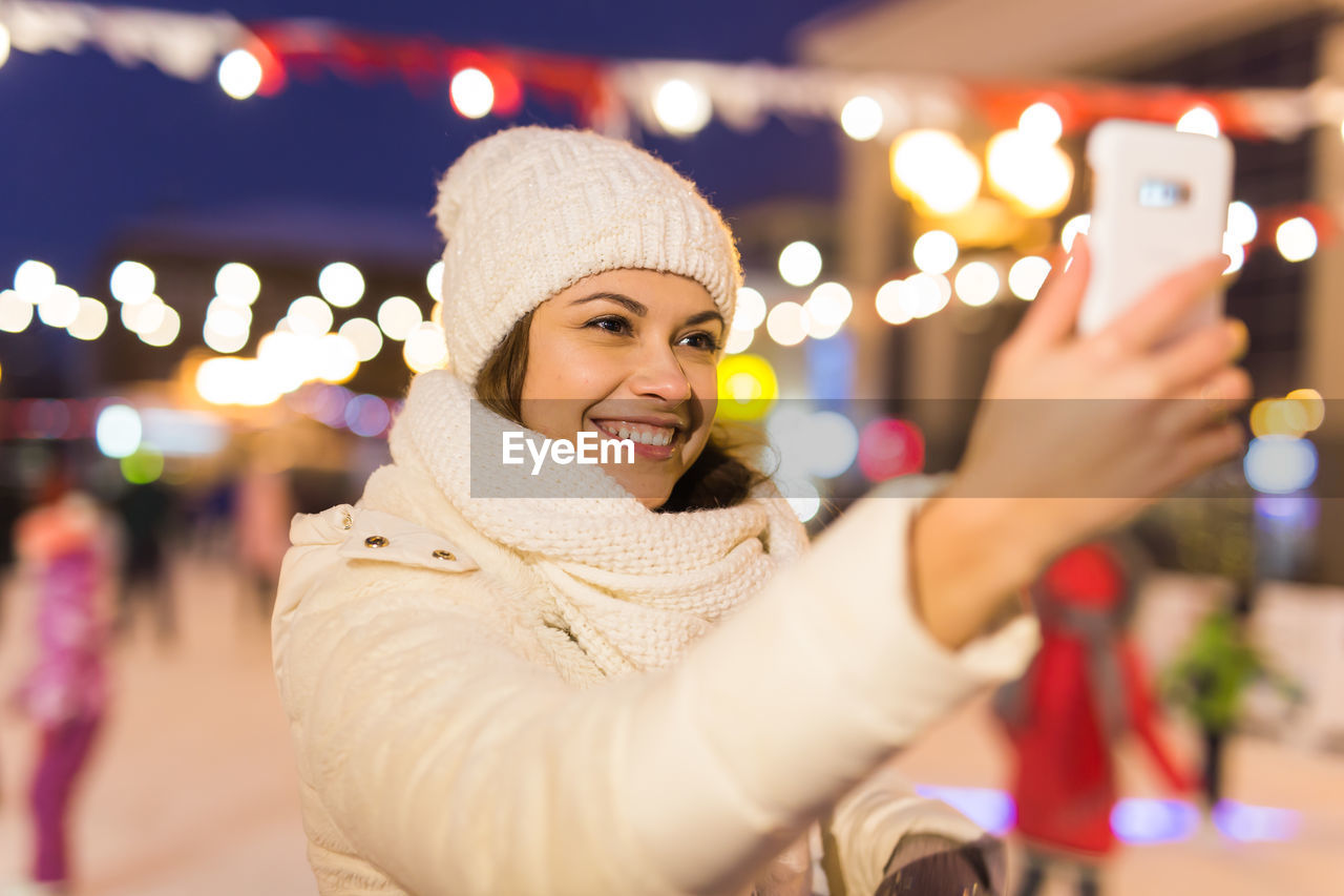 portrait of smiling young woman standing in city at night