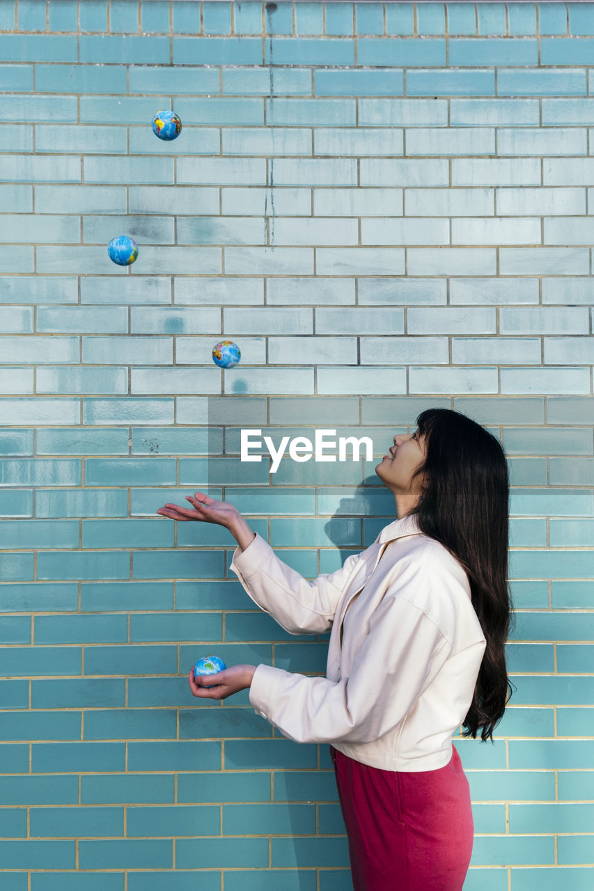 Young woman juggling with globes by turquoise brick wall