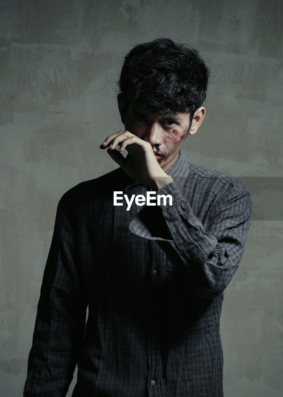 Portrait of injured young man standing against wall