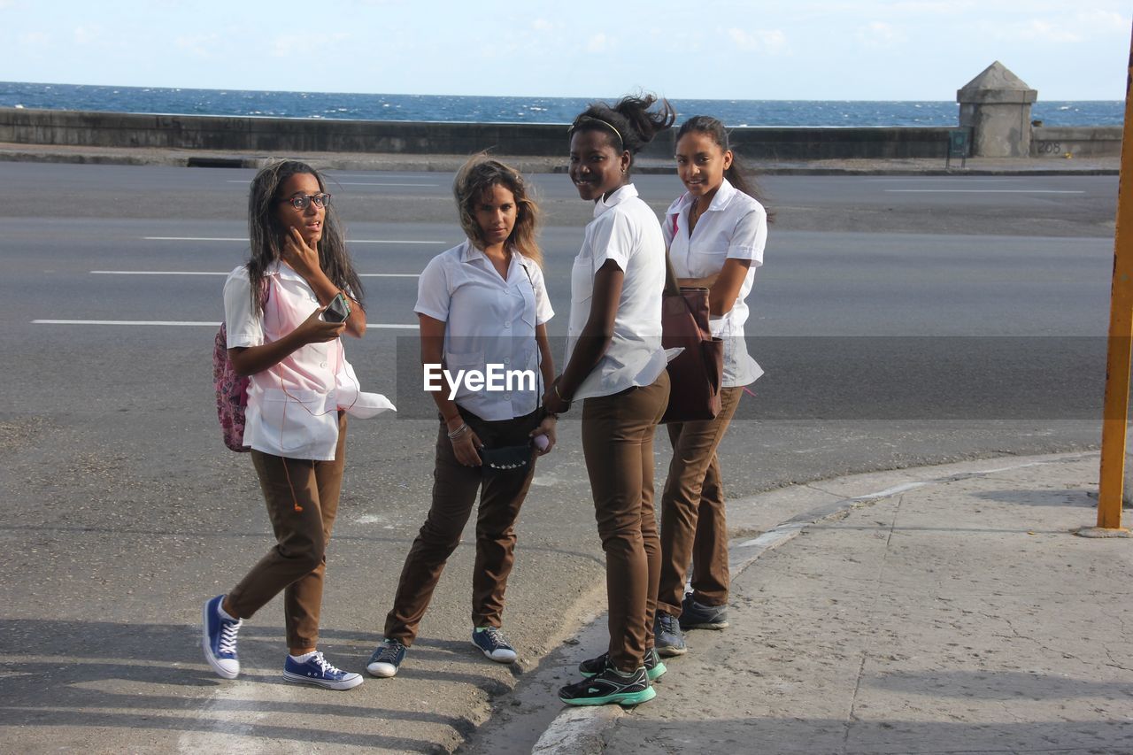 REAR VIEW OF PEOPLE STANDING ON ROAD ALONG THE SEA