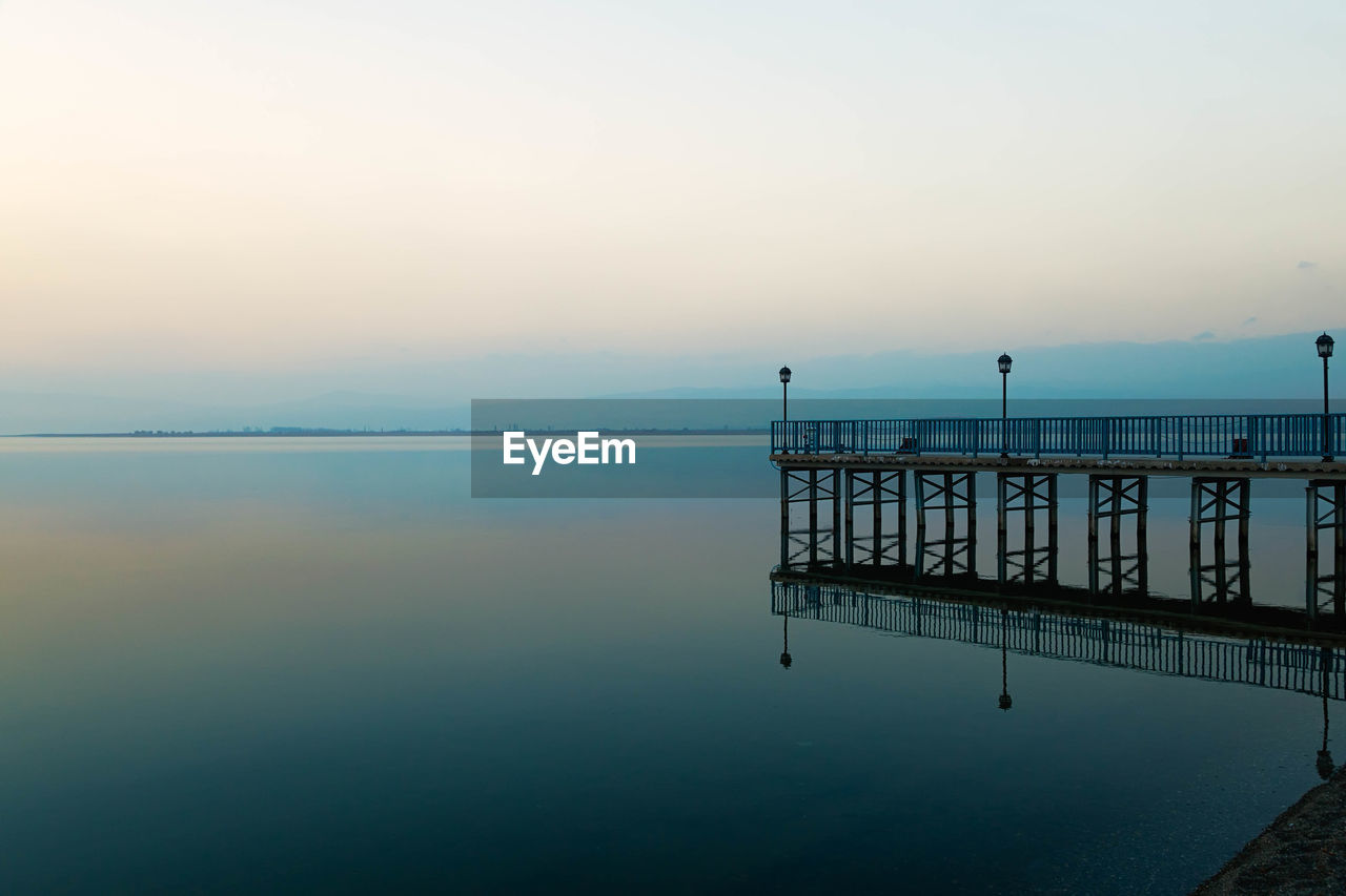 Pier by calm lake against sky