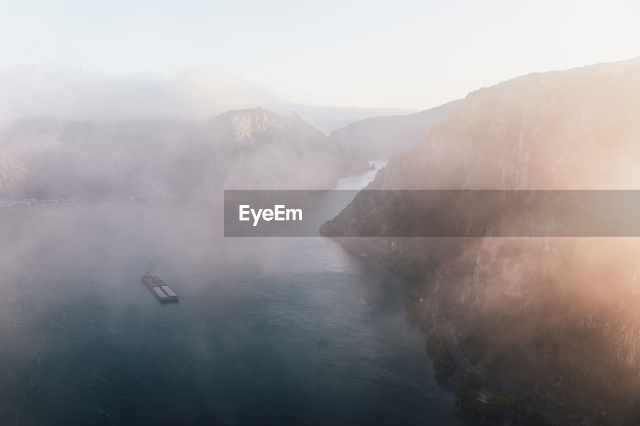 Majestic foggy autumn landscape with cargo ship on water at sunrise . danube river, gorge