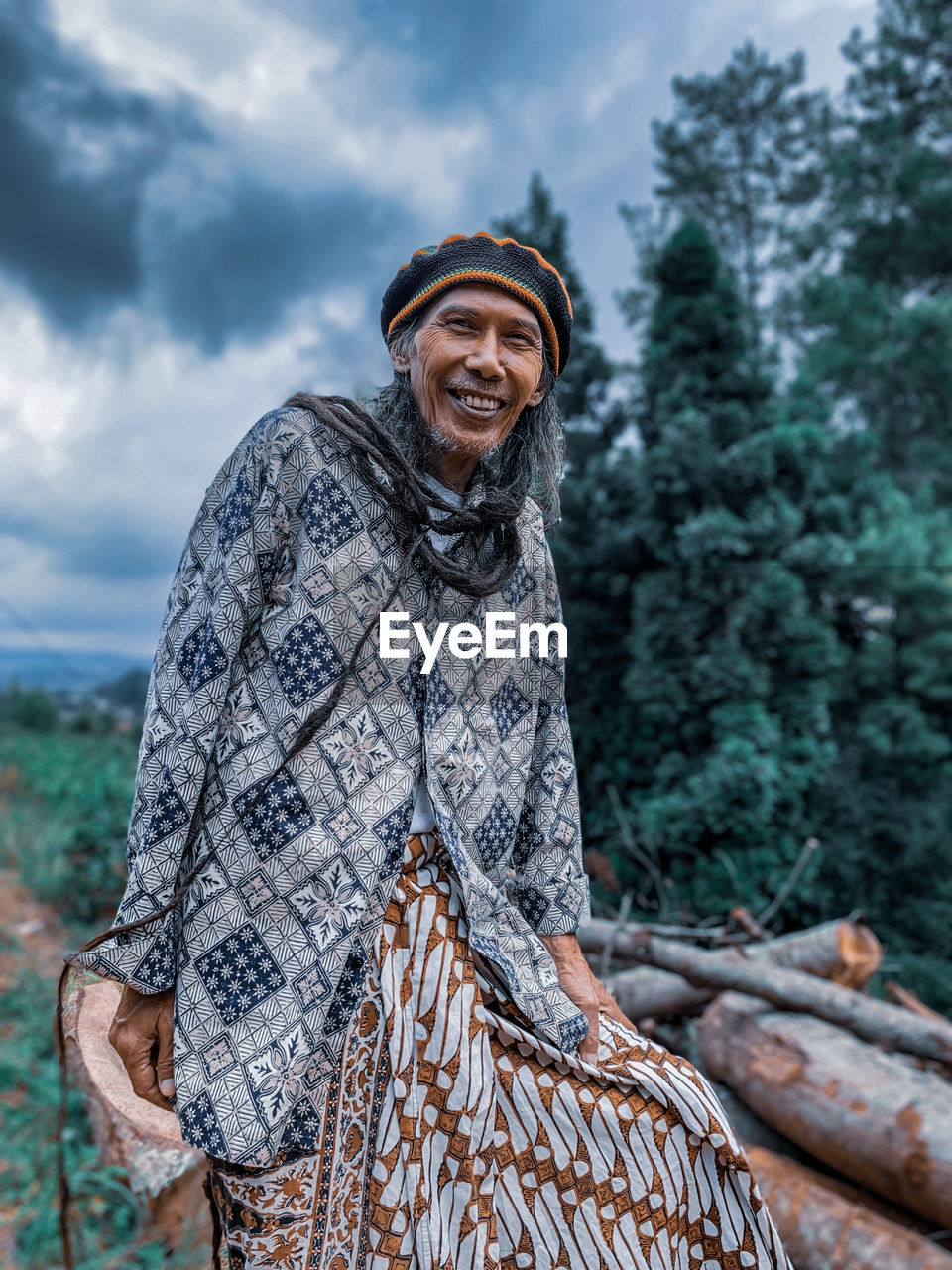 An old man with dreadlocks wearing a batik outfit.with a reggae hat.posing in front of the camera