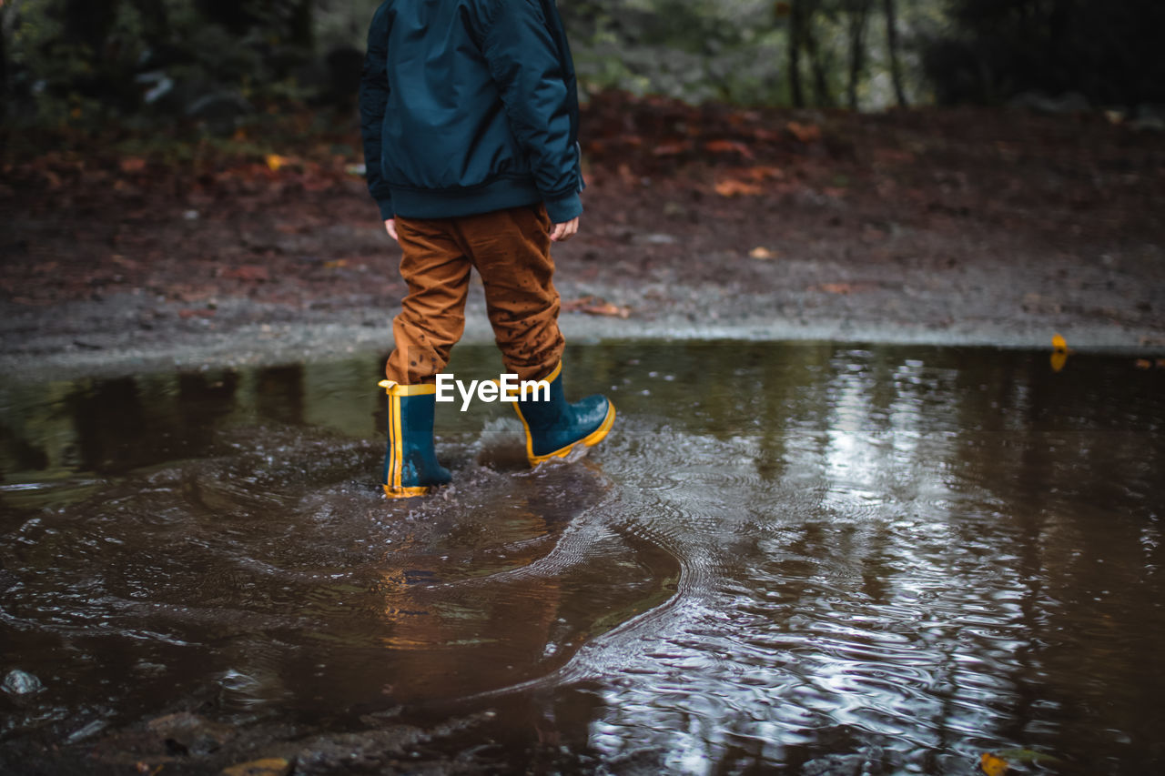 Low section of boy wearing boots while walking in puddle in forest