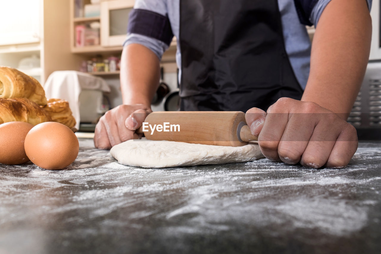 Midsection of man rolling dough on table 