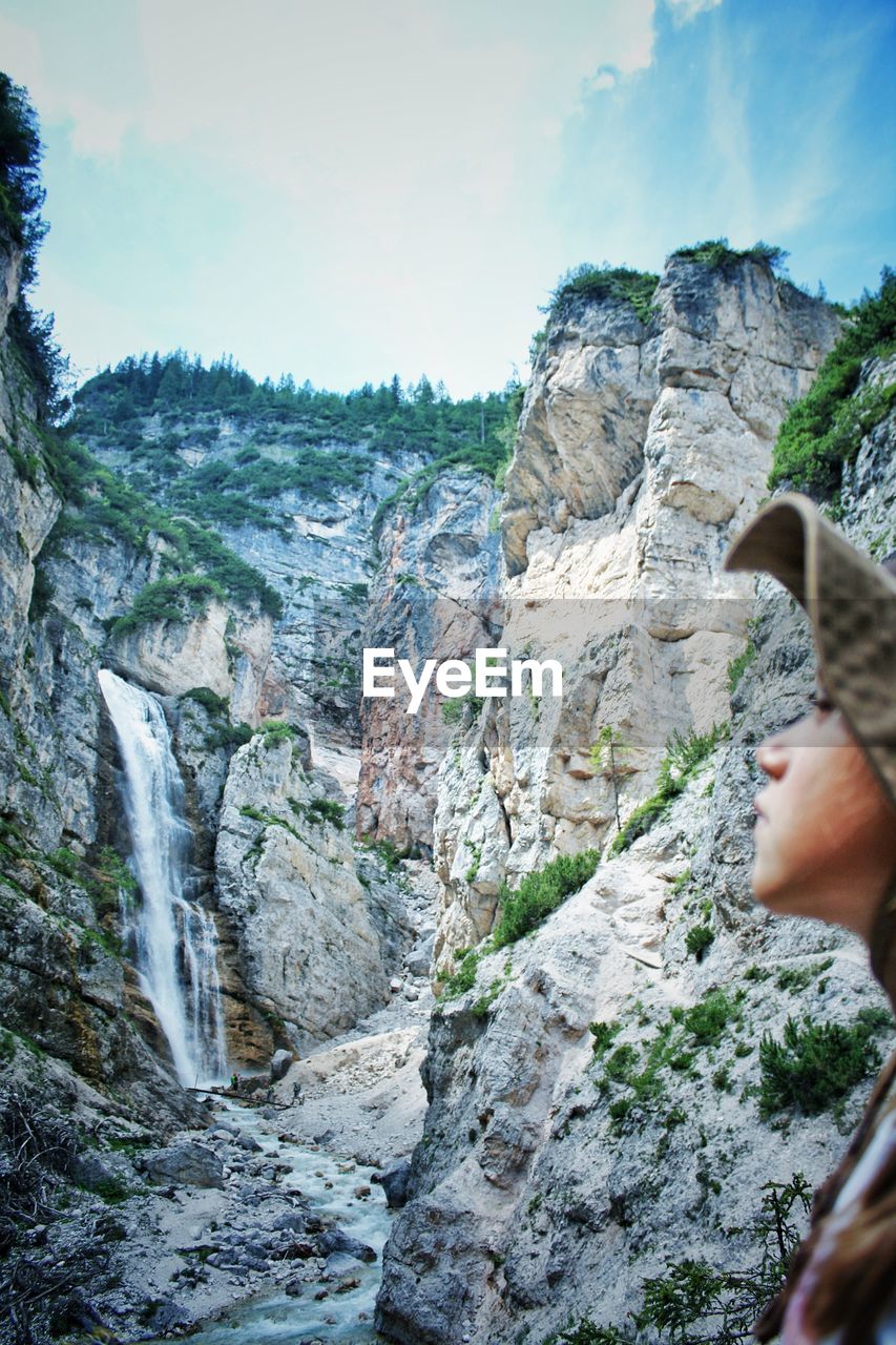 REAR VIEW OF MAN ON ROCK AGAINST ROCKY MOUNTAIN