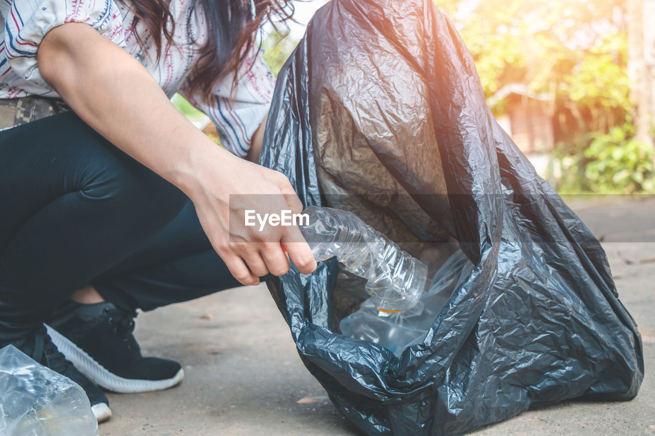 Low section of woman collecting garbage in plastic bag on road