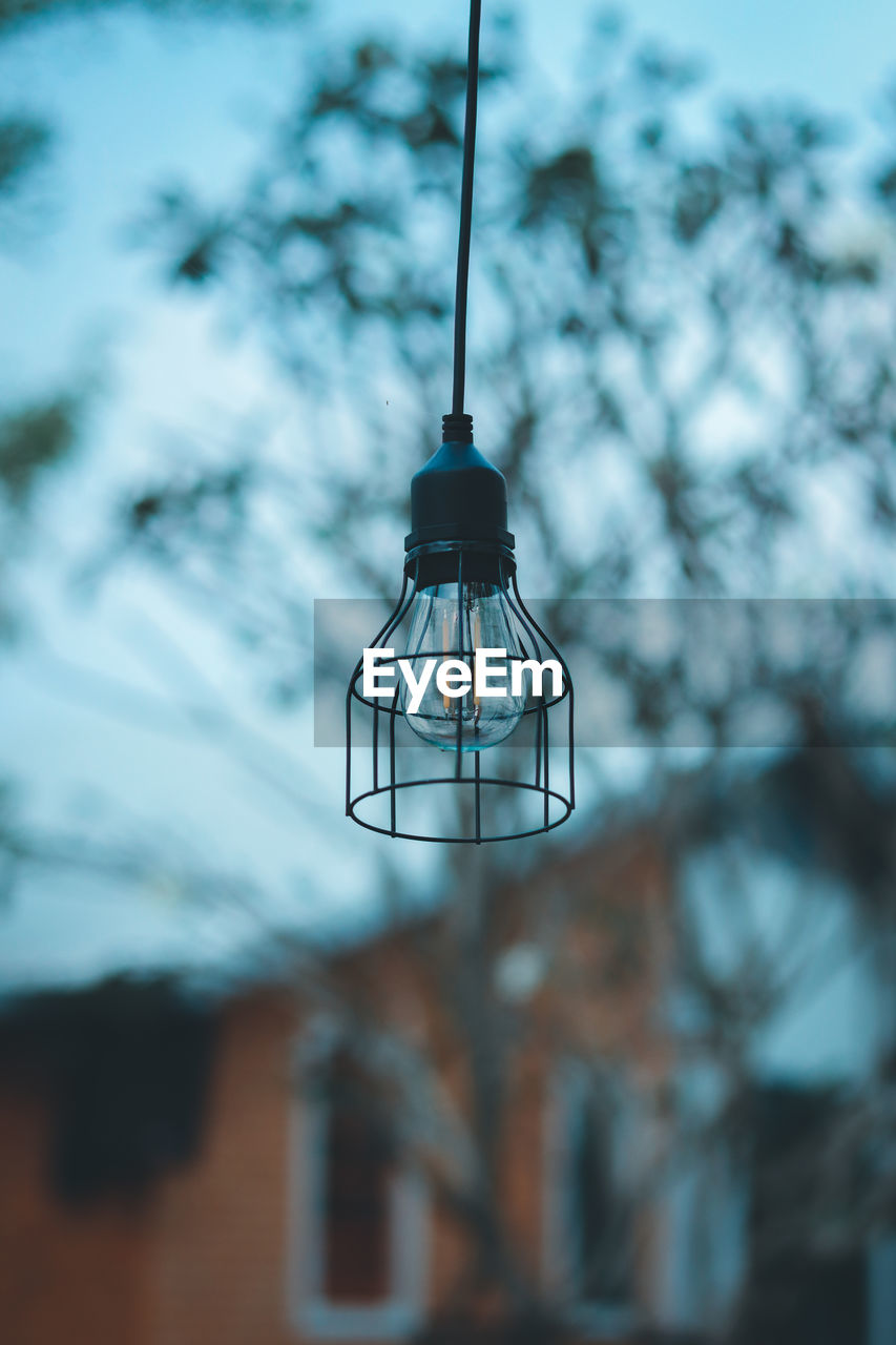  low angle view of illuminated light bulb hanging against sky at dusk