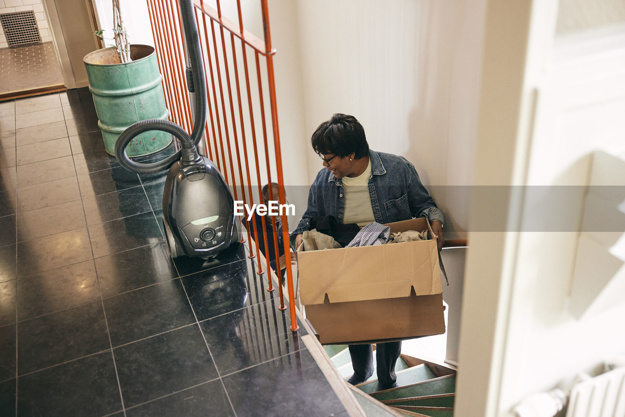 Senior woman carrying cardboard box while moving on stairs at home