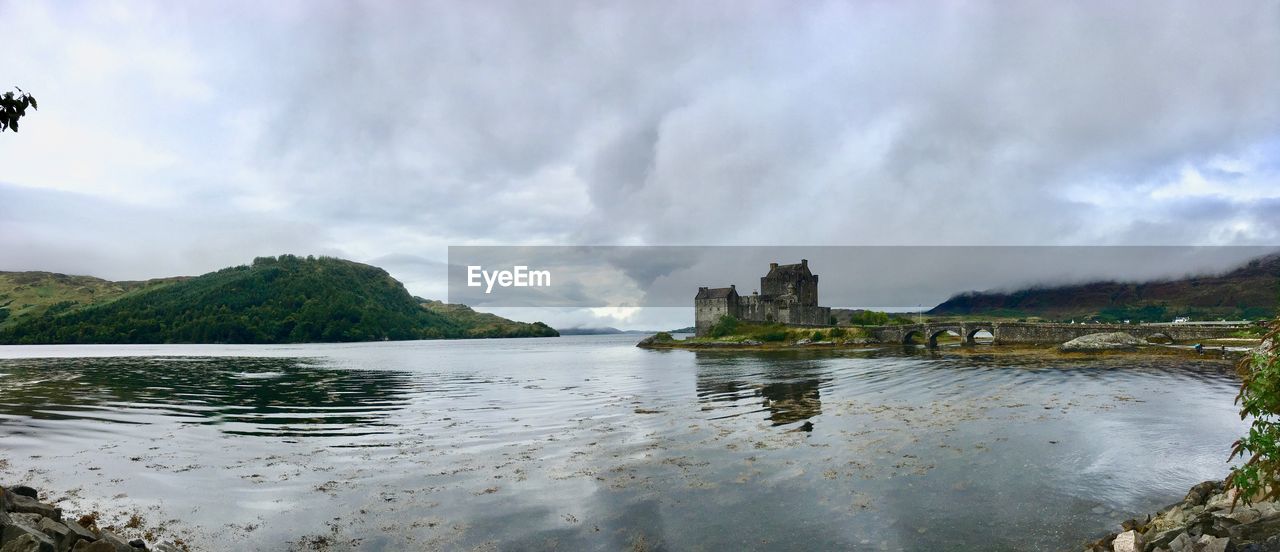 Castle by lake against cloudy sky