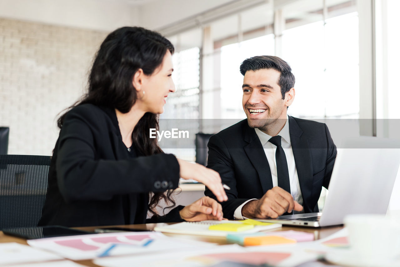 SMILING YOUNG COUPLE WITH HANDS ON TABLE AT HOME