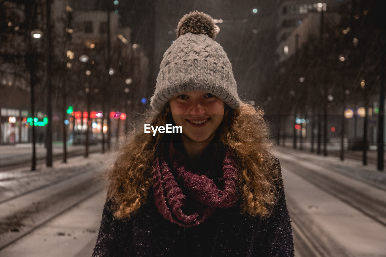 Portrait of smiling young woman standing in city during winter