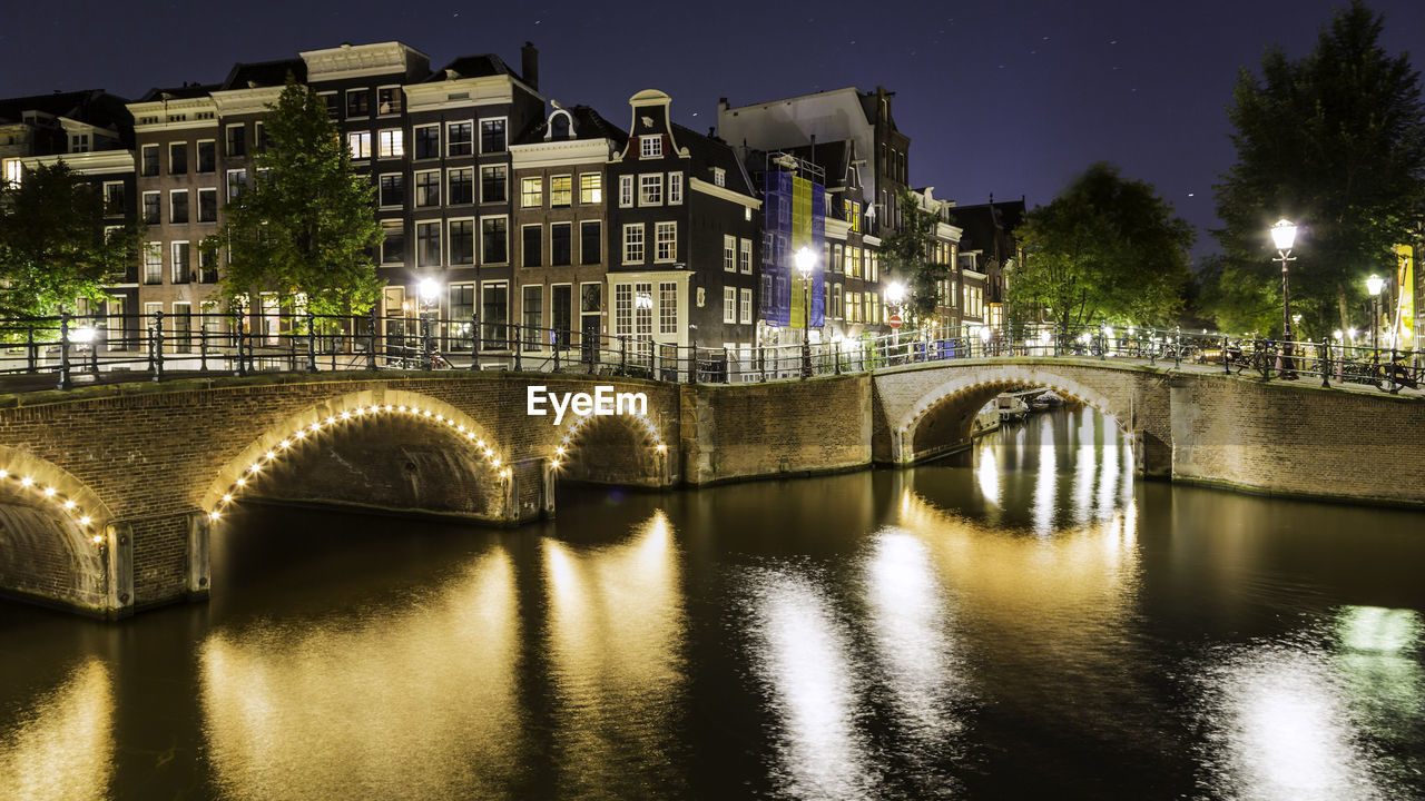 Illuminated arch bridge over river in city at dusk