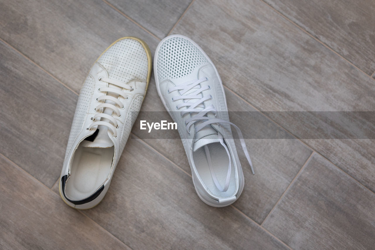 Pair of trendy new and old white shoes on light wooden background, top view