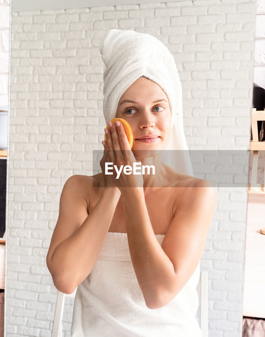 Happy smiling young woman in white bath towels doing morning make up looking at the mirror