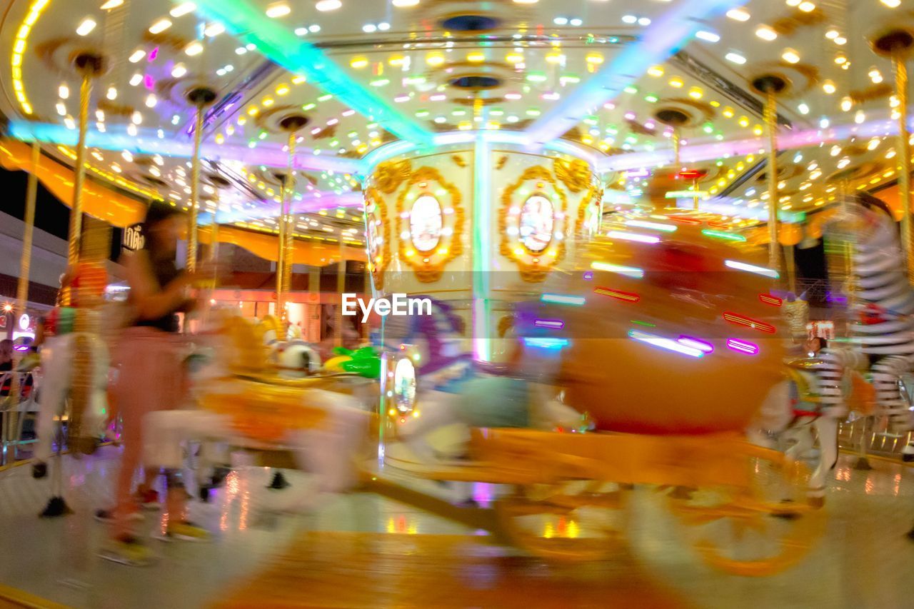 BLURRED MOTION OF CAROUSEL IN AMUSEMENT PARK AT NIGHT