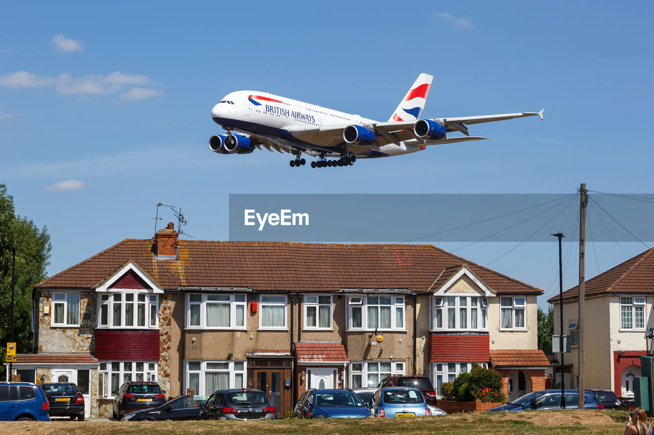 AIRPLANE FLYING BY BUILDINGS AGAINST SKY