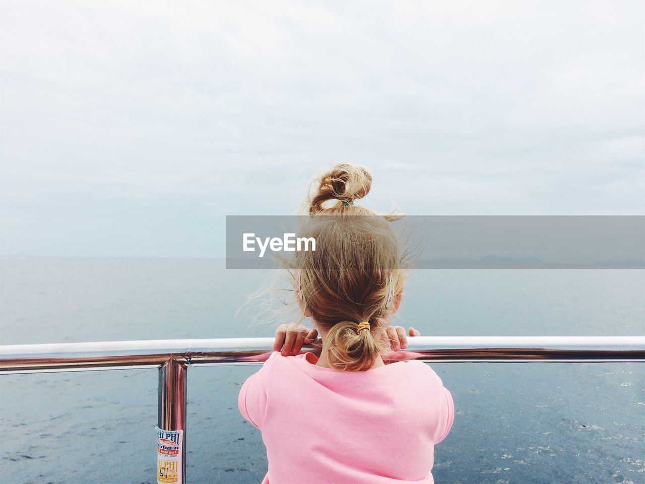 Rear view of girl standing by railing at sea against sky