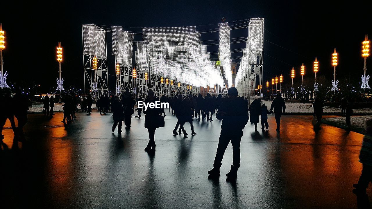 CROWD ON ILLUMINATED STREET AT NIGHT