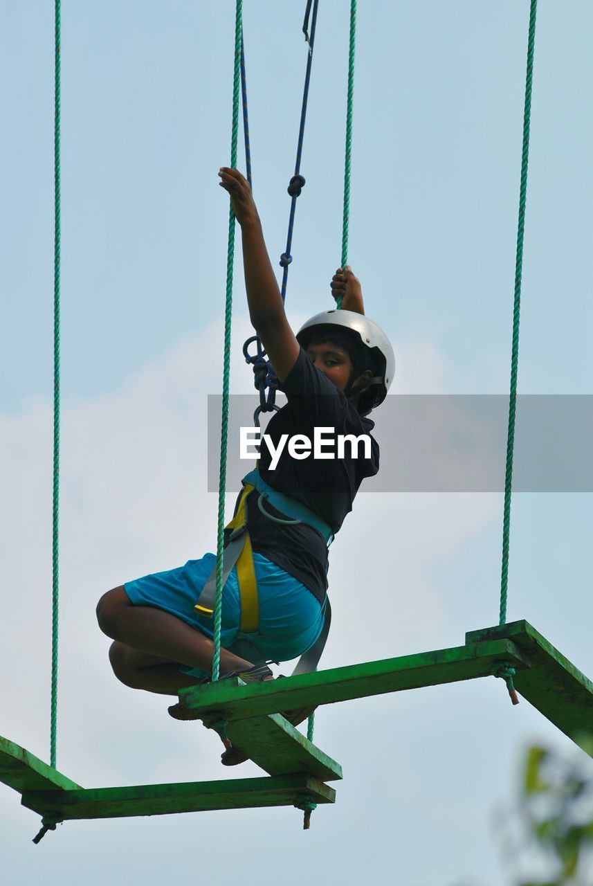 Low angle view of boy zip lining against sky