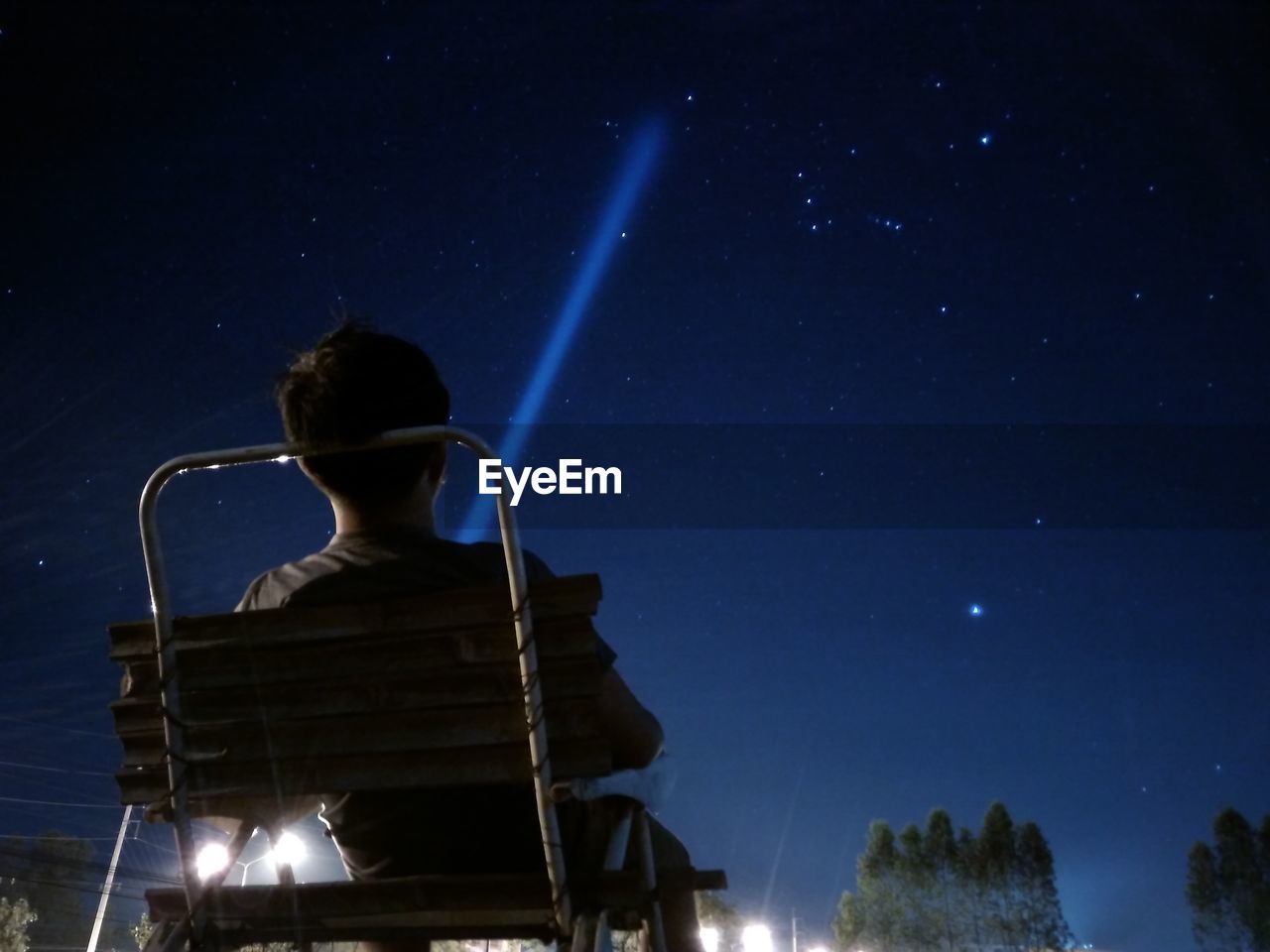 Rear view of man with flashlight against star field at night