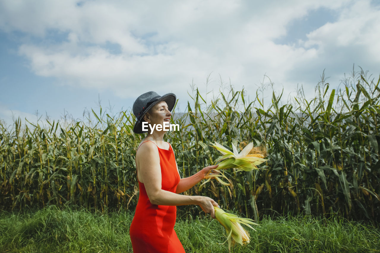 Woman wearing hat and red dress juggling corns walking at field