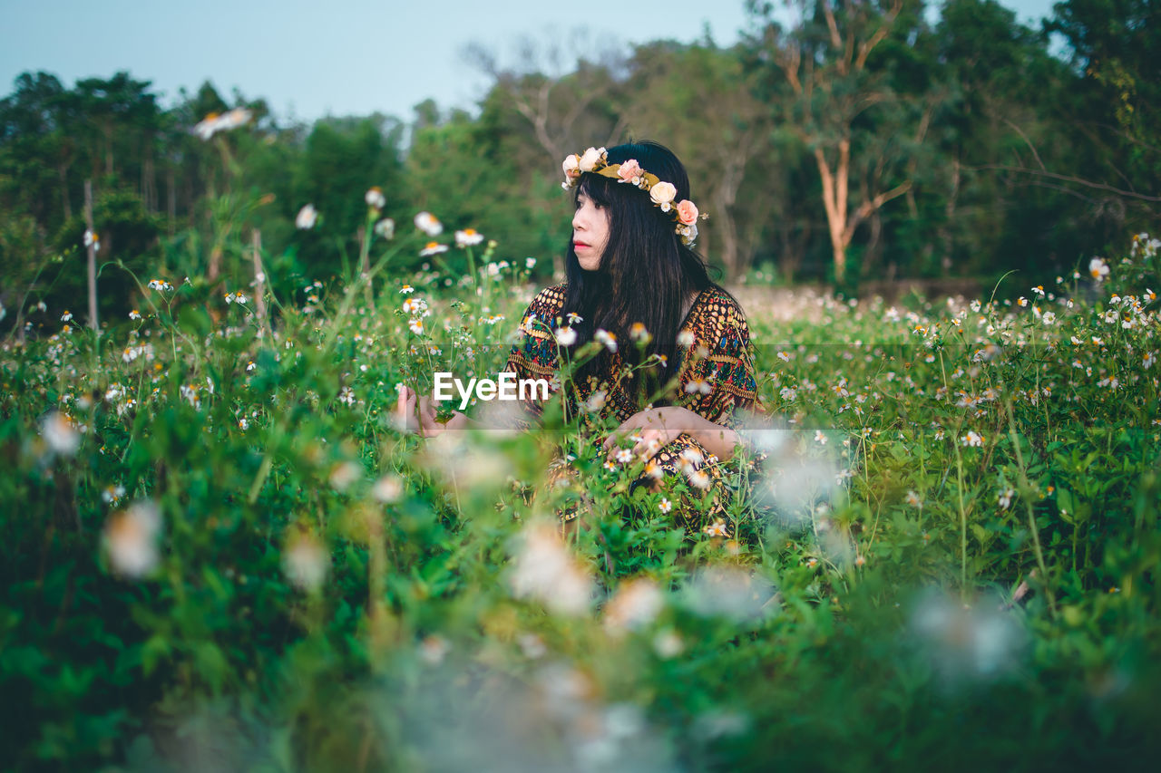 Woman wearing flowers while sitting on field 