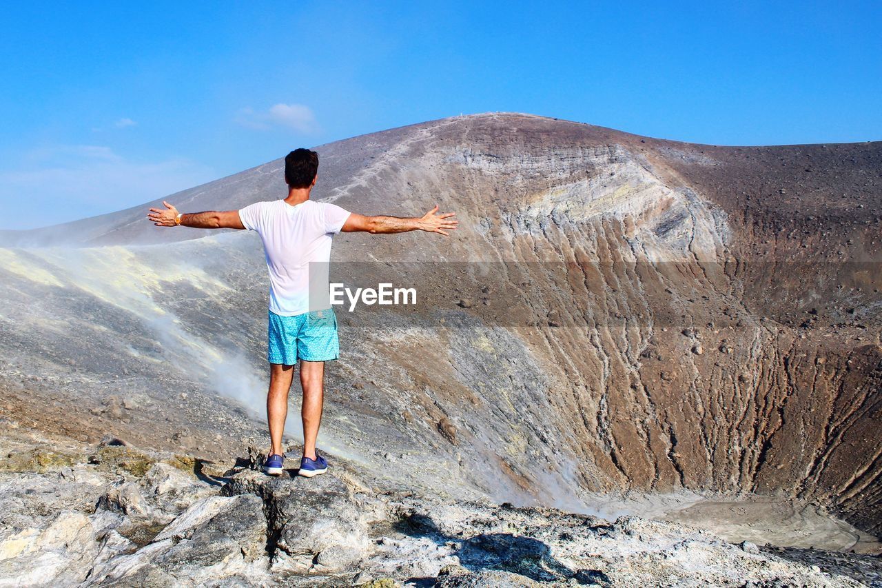 Rear view of man with arms outstretched standing at volcano