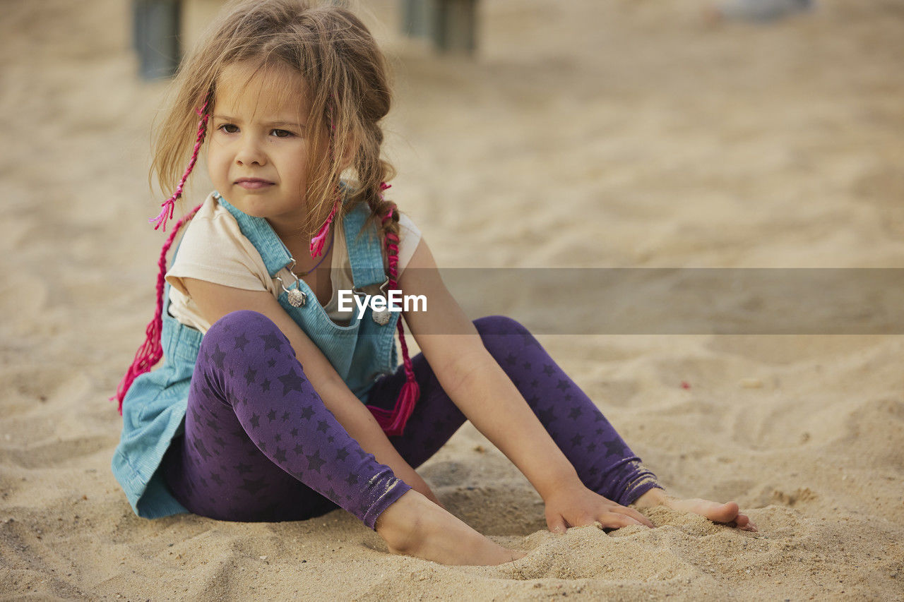 full length of young woman sitting on sand at beach
